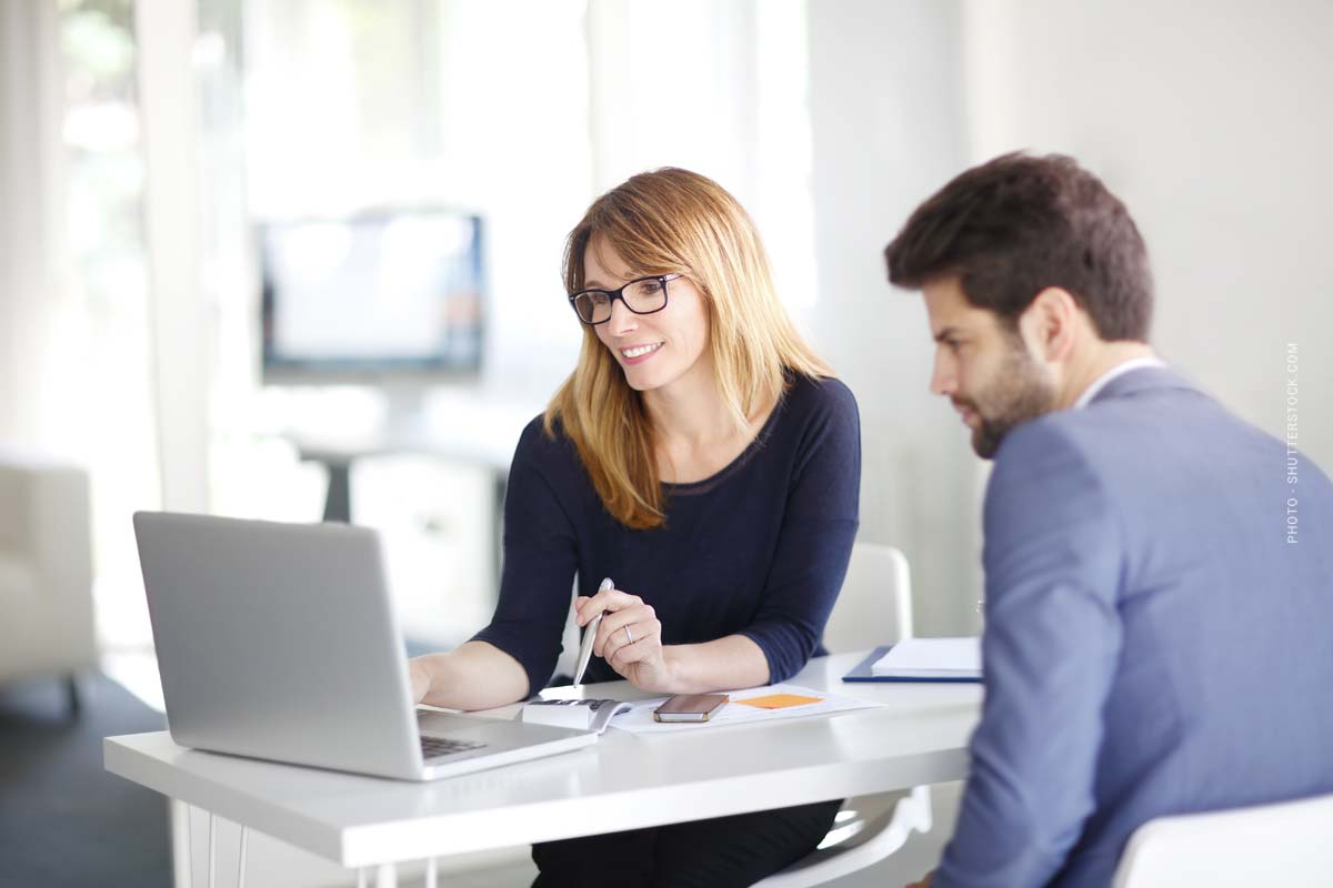 Finanzierungsvermittlerin beratet einen Kunden in ihrem Büro. Beide sehen gespannt auf den Laptop und erstellen einen Finanzplan, der zum Kunden passt.