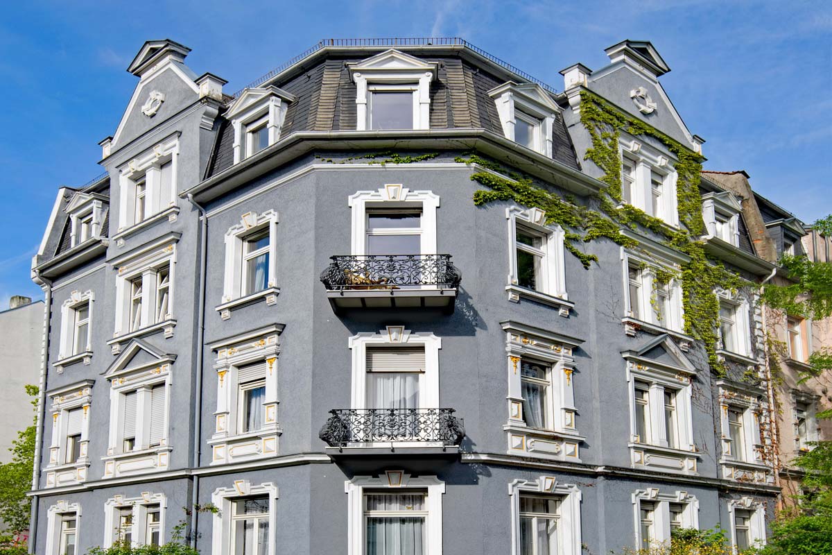 mietverwaltung-hausverwaltung-definition-aufgaben-arten-vertrag-kosten-ratgeber-tipps-mehrfamilienhaus-altbau-fassade-blau-balkon-fenster-himmel