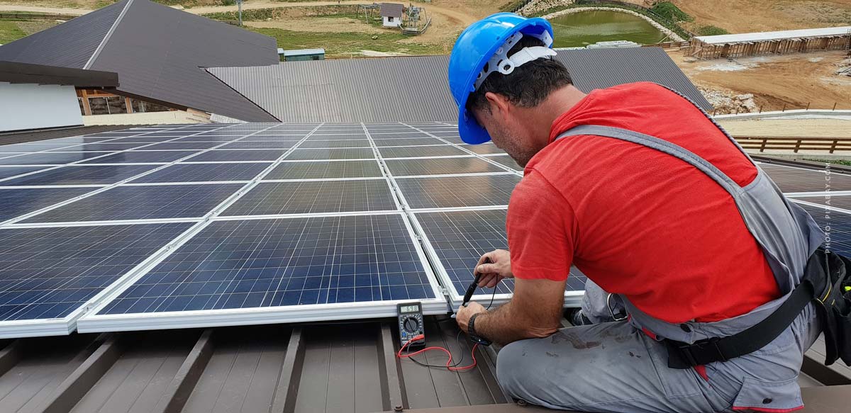 photovoltaic-solar-energie-installateur-installation-elektro-elektroinstallateur-auf-dach-rotes-tshirt-schraubt-an-neuer-solaranlage